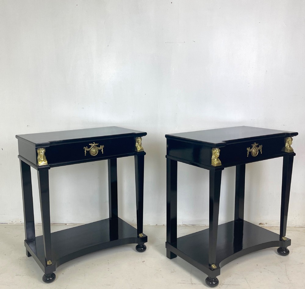 A pair of ebonised black side tables featuring single drawers, lower shelves, and gilt brass mounts on square legs. View V