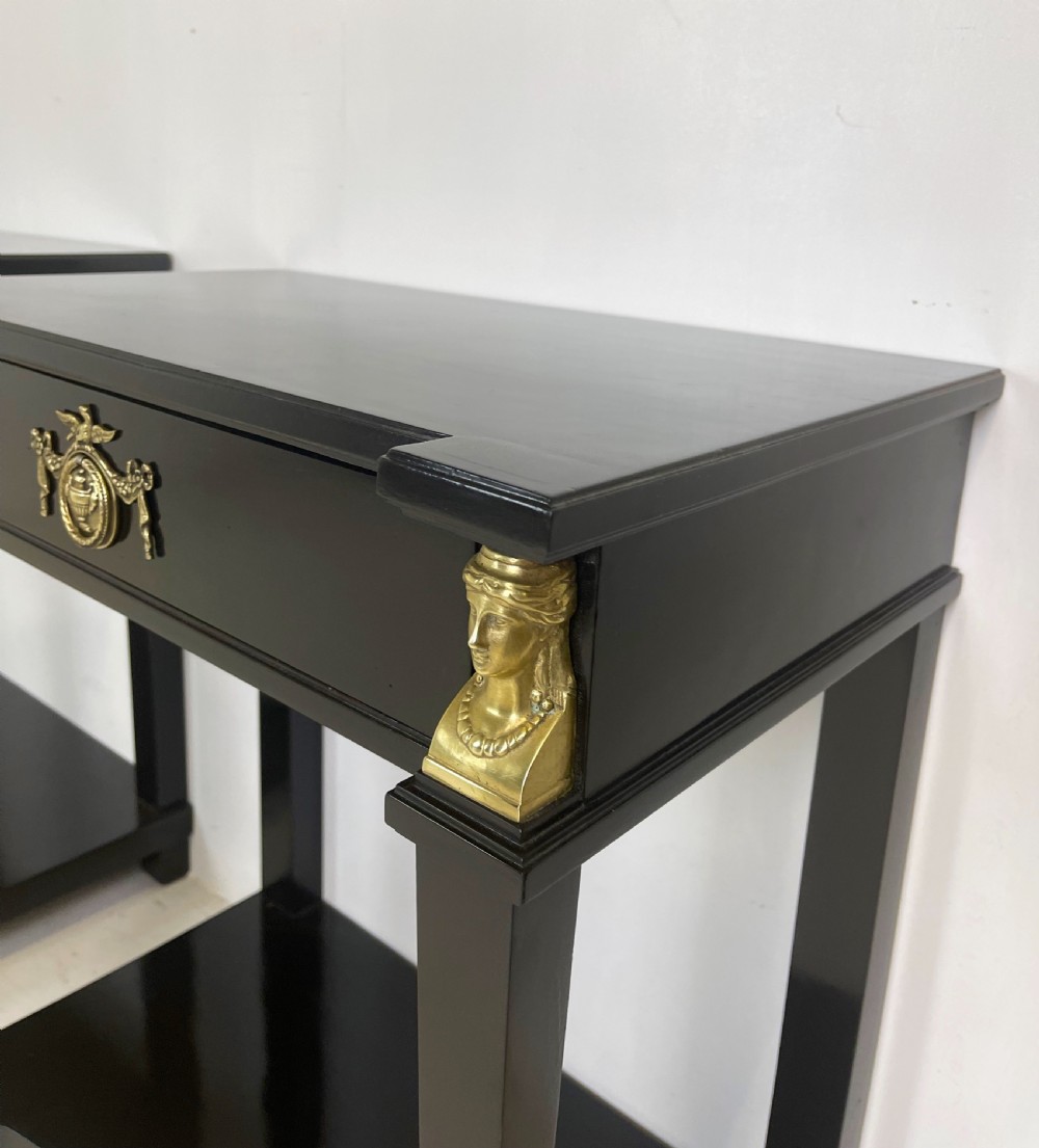 A pair of ebonised black side tables featuring single drawers, lower shelves, and gilt brass mounts on square legs. View VI