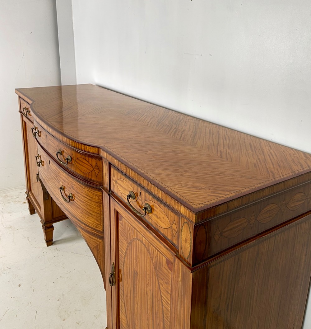 An Edwardian satinwood sideboard featuring oval marquetry inlays, drawers, two side cupboard doors, and tapered legs. View VI