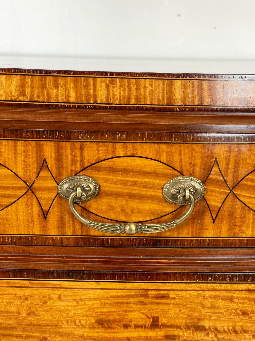An Edwardian satinwood sideboard featuring oval marquetry inlays, drawers, two side cupboard doors, and tapered legs. View VII