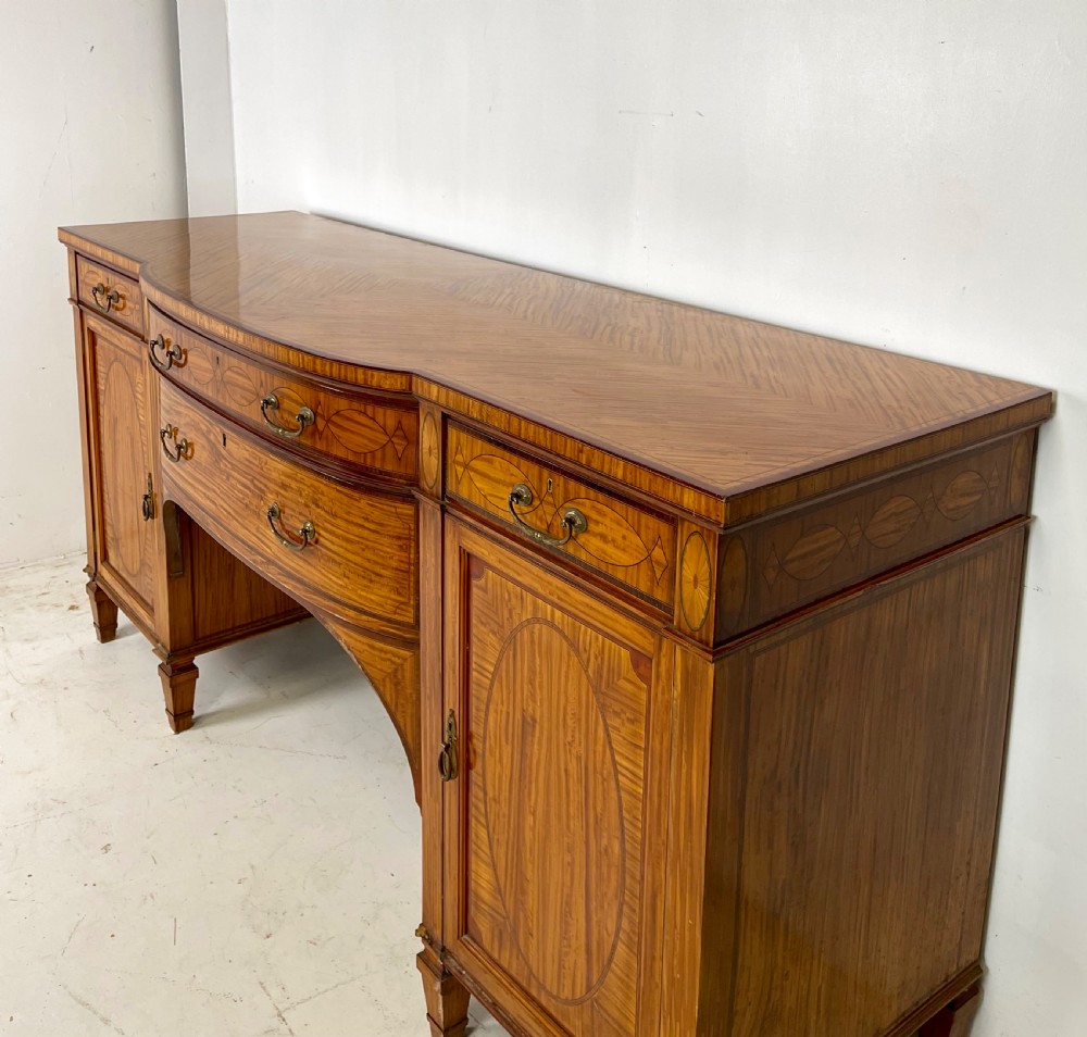 An Edwardian satinwood sideboard featuring oval marquetry inlays, drawers, two side cupboard doors, and tapered legs. View VIII