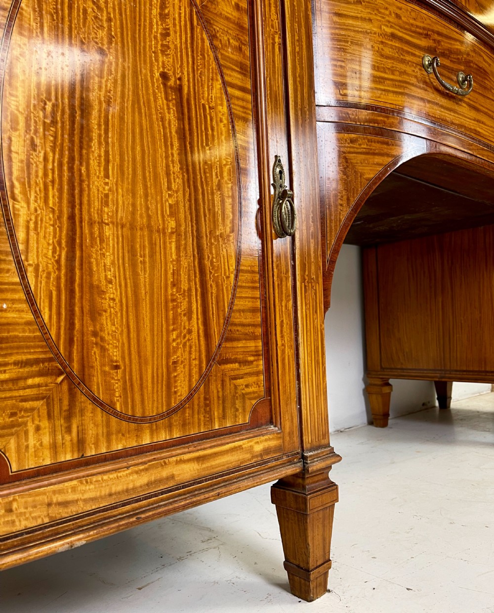 An Edwardian satinwood sideboard featuring oval marquetry inlays, drawers, two side cupboard doors, and tapered legs. View IX