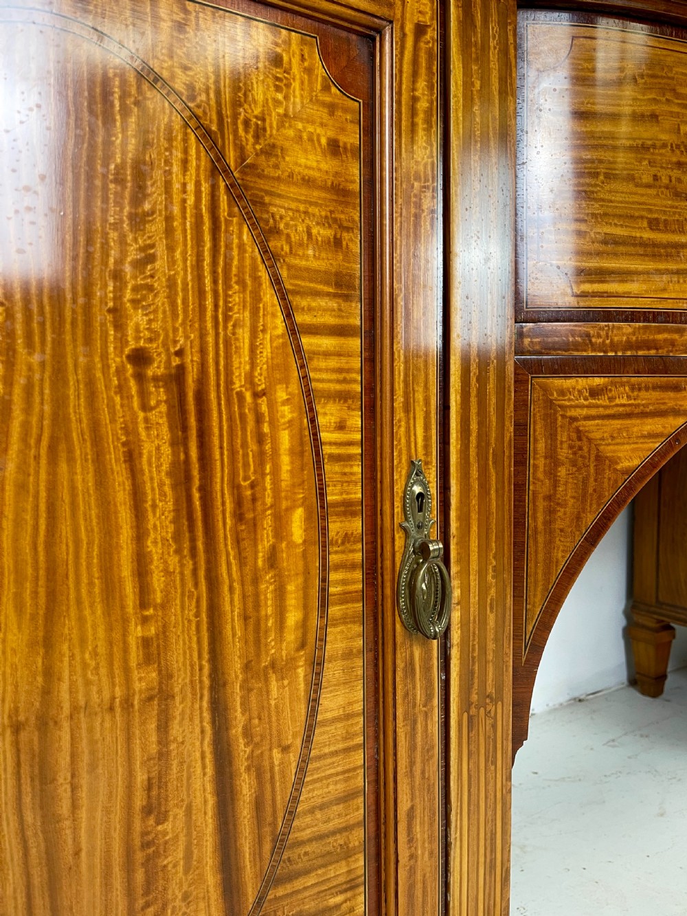 An Edwardian satinwood sideboard featuring oval marquetry inlays, drawers, two side cupboard doors, and tapered legs. View X