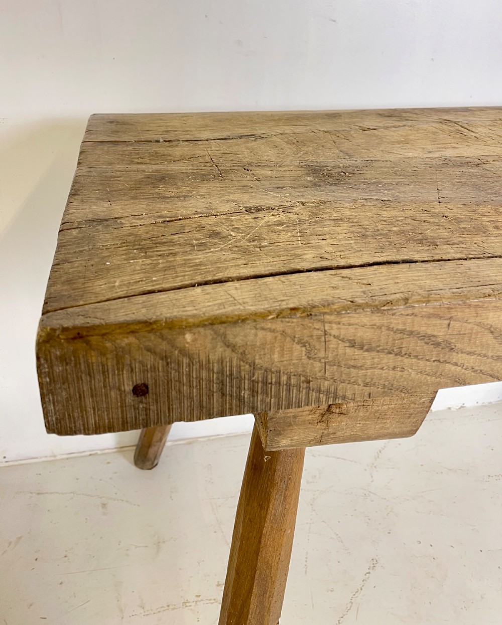 An antique rustic wooden work table featuring a thick timber top supported by four splayed cylindrical legs with visible wear and grain. View V