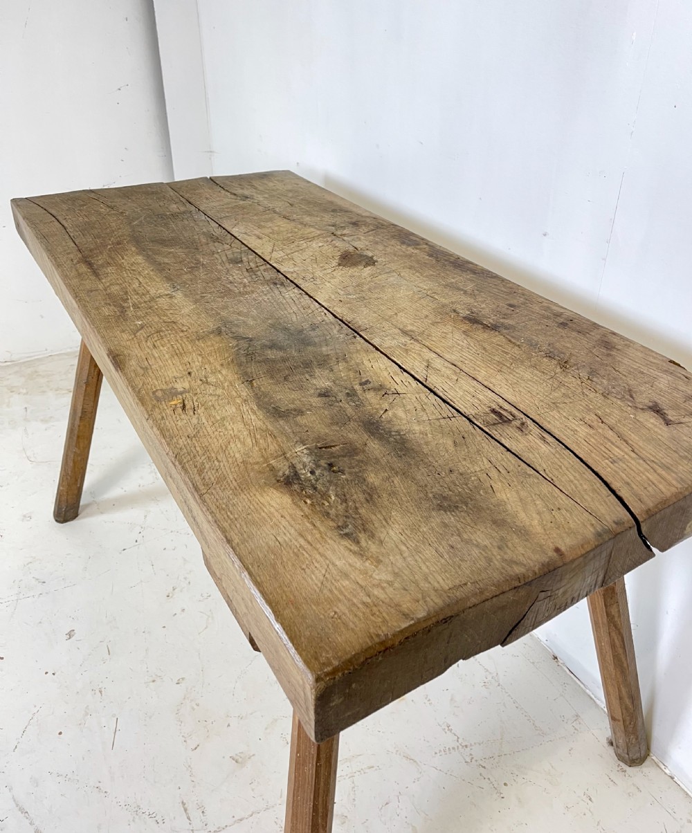 An antique rustic wooden work table featuring a thick timber top supported by four splayed cylindrical legs with visible wear and grain. View VII