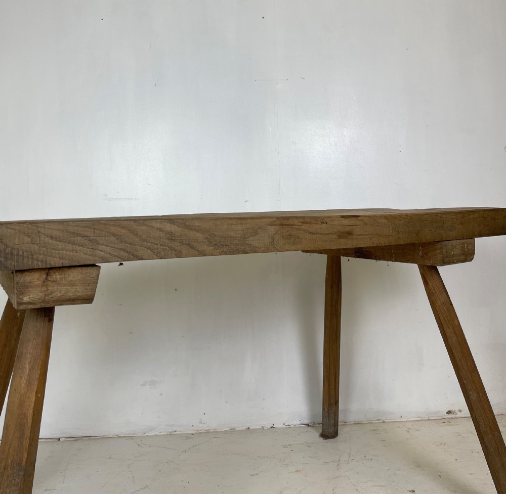 An antique rustic wooden work table featuring a thick timber top supported by four splayed cylindrical legs with visible wear and grain. View IX
