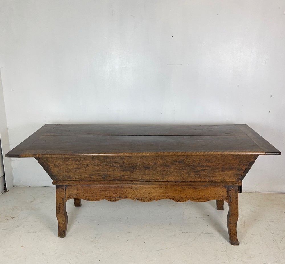 An antique French walnut dough bin featuring a flat overhanging top, sloped timber sides, and a scalloped apron resting on short legs. View II