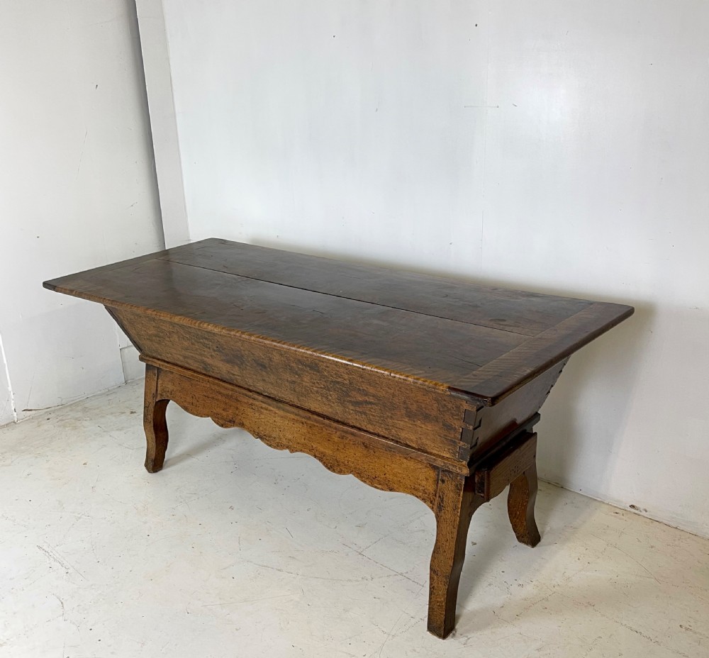 An antique French walnut dough bin featuring a flat overhanging top, sloped timber sides, and a scalloped apron resting on short legs. View III