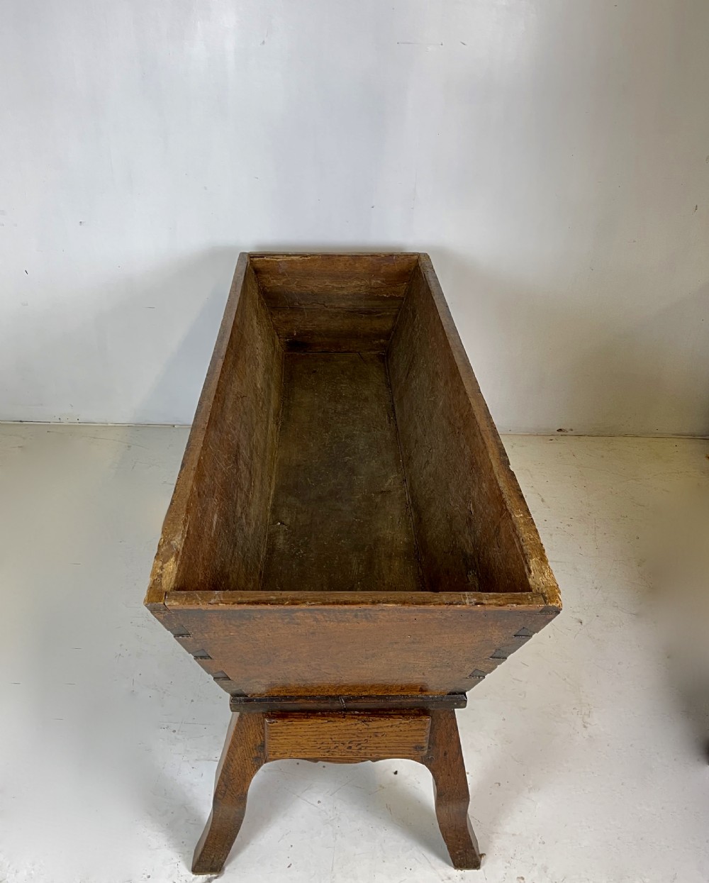 An antique French walnut dough bin featuring a flat overhanging top, sloped timber sides, and a scalloped apron resting on short legs. View VI