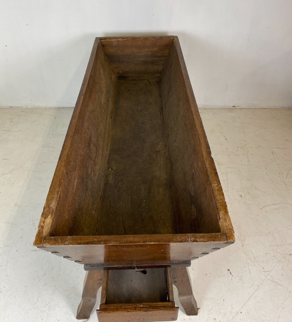 An antique French walnut dough bin featuring a flat overhanging top, sloped timber sides, and a scalloped apron resting on short legs. View IX