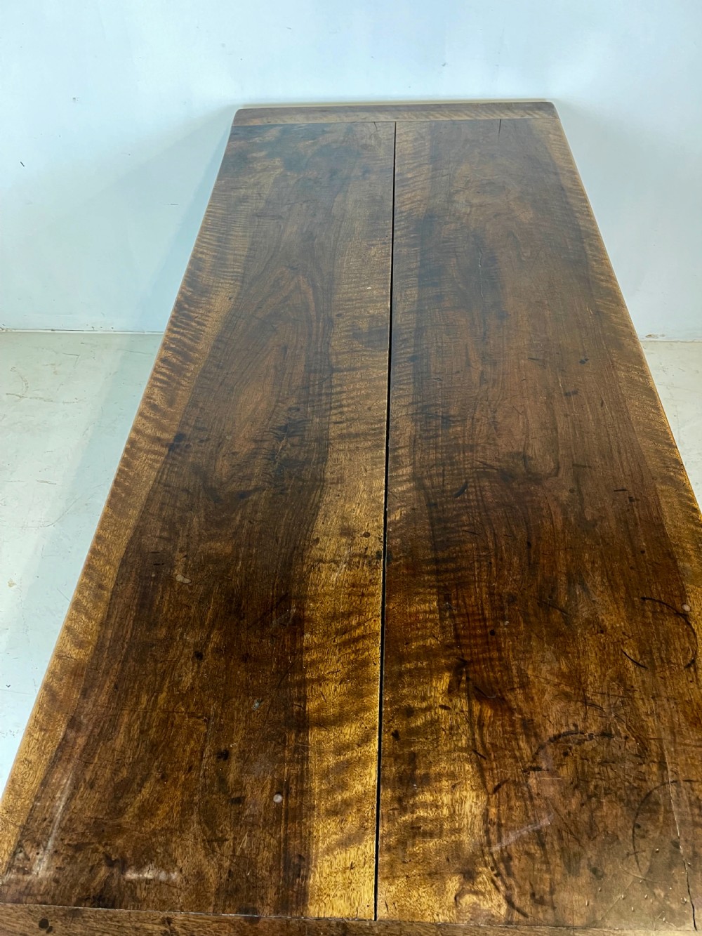 An antique French walnut dough bin featuring a flat overhanging top, sloped timber sides, and a scalloped apron resting on short legs. View XII