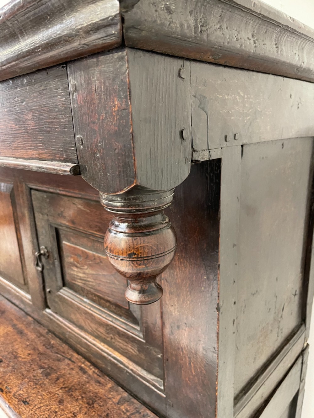 A dark oak joined court cupboard featuring a recessed upper section with geometric panelled doors and turned drop finials above a two-door base. View III