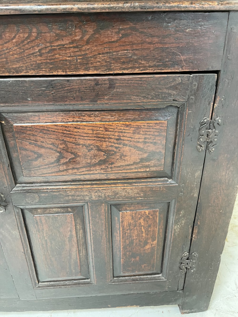 A dark oak joined court cupboard featuring a recessed upper section with geometric panelled doors and turned drop finials above a two-door base. View IV