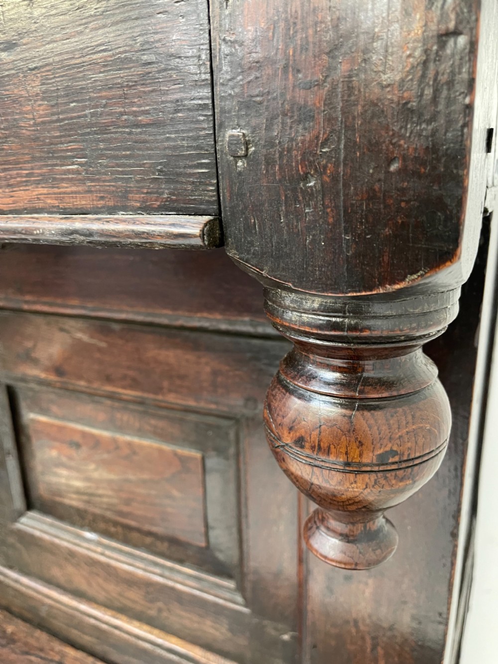 A dark oak joined court cupboard featuring a recessed upper section with geometric panelled doors and turned drop finials above a two-door base. View V