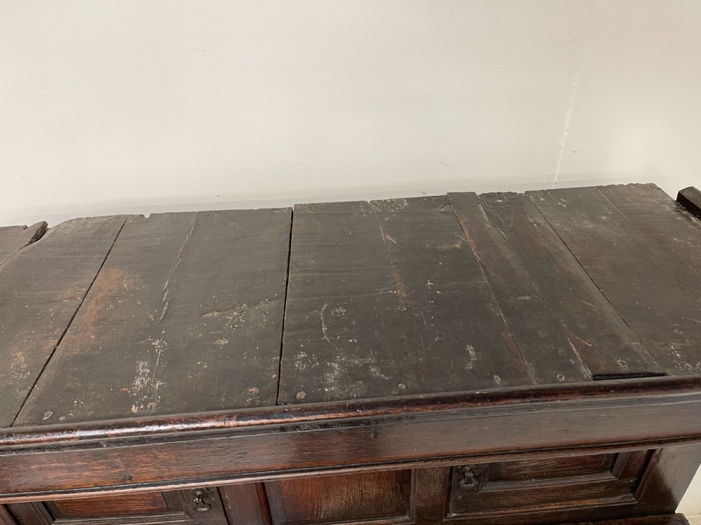 A dark oak joined court cupboard featuring a recessed upper section with geometric panelled doors and turned drop finials above a two-door base. View VII