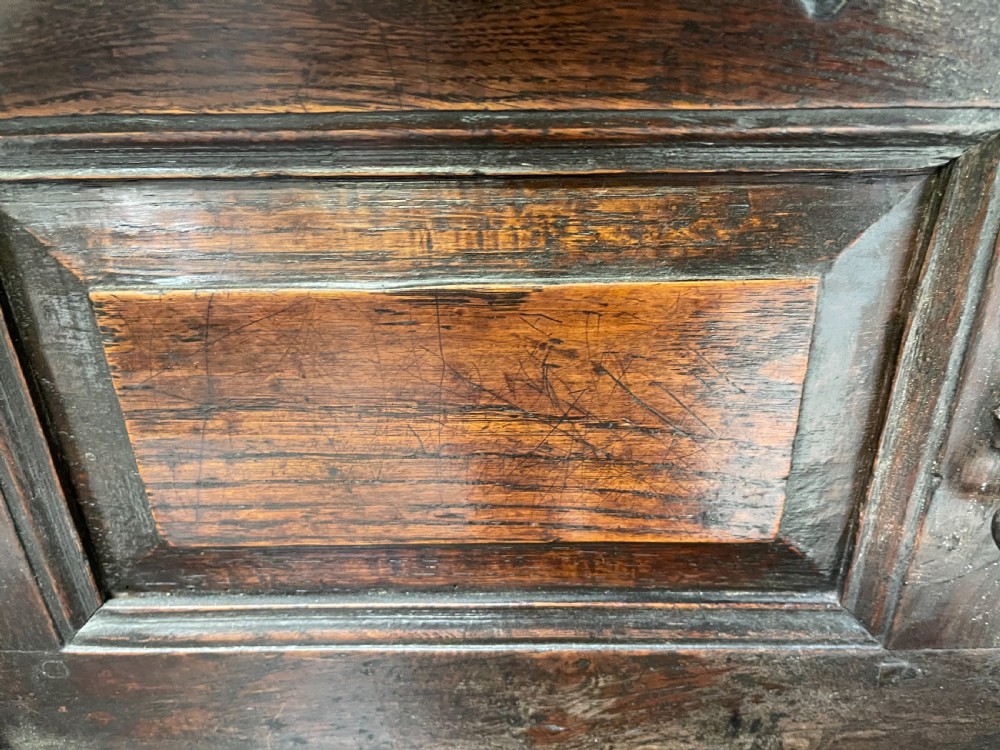 A dark oak joined court cupboard featuring a recessed upper section with geometric panelled doors and turned drop finials above a two-door base. View IX
