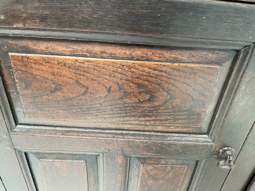 A dark oak joined court cupboard featuring a recessed upper section with geometric panelled doors and turned drop finials above a two-door base. View X