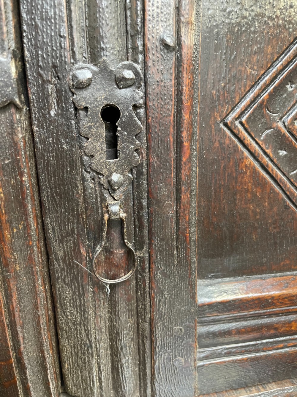A dark carved oak court cupboard featuring upper and lower double doors with geometric diamond panels, guilloche frieze carving, and turned side supports. View IV