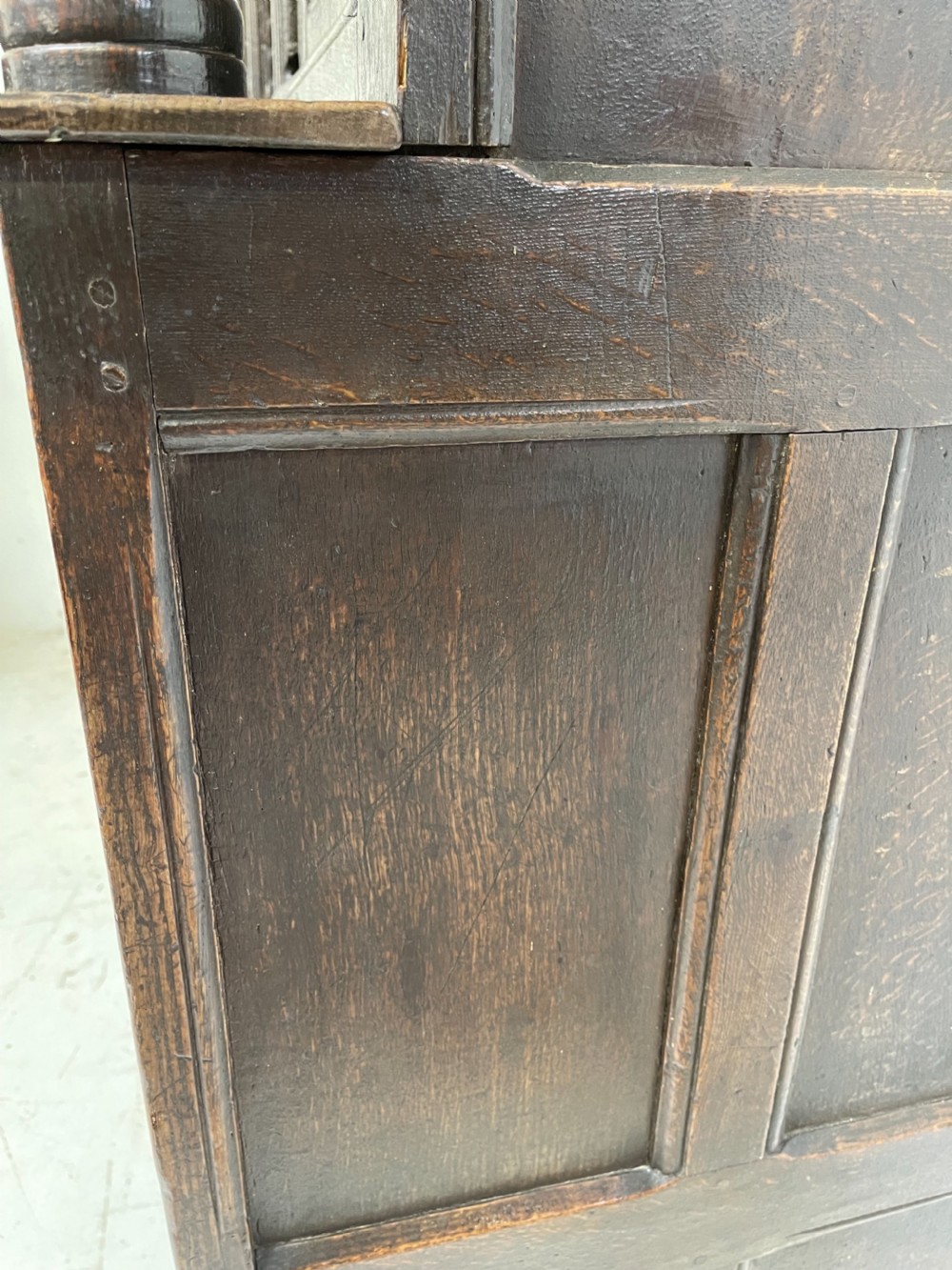 A dark carved oak court cupboard featuring upper and lower double doors with geometric diamond panels, guilloche frieze carving, and turned side supports. View VIII
