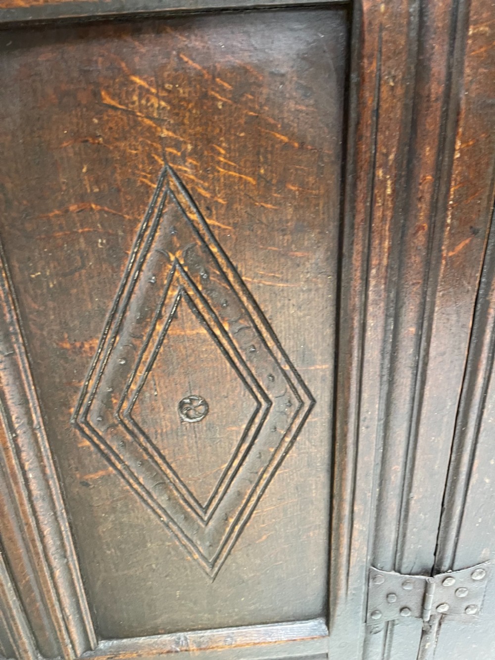 A dark carved oak court cupboard featuring upper and lower double doors with geometric diamond panels, guilloche frieze carving, and turned side supports. View XII