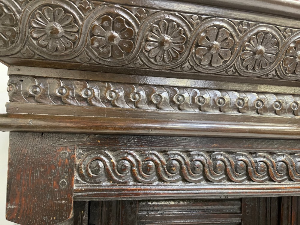 A dark carved oak court cupboard featuring upper and lower double doors with geometric diamond panels, guilloche frieze carving, and turned side supports. View XIII