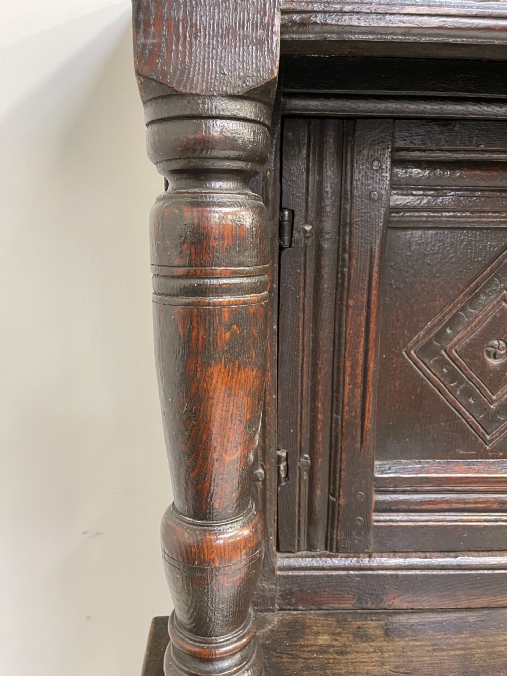 A dark carved oak court cupboard featuring upper and lower double doors with geometric diamond panels, guilloche frieze carving, and turned side supports. View XV