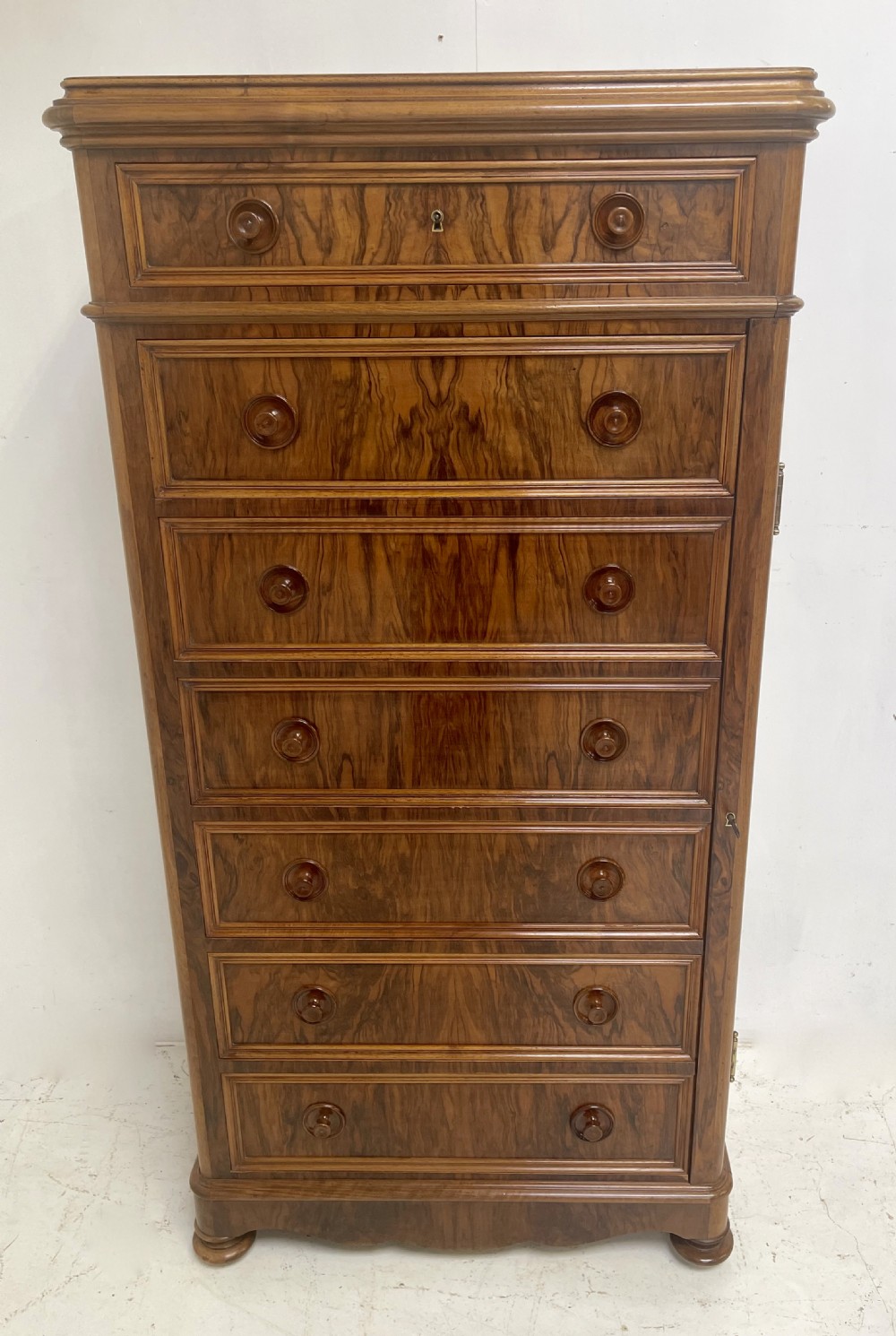 A tall Victorian walnut Wellington chest with seven graduated drawers, turned wooden knobs, and a hinged side-locking bar.