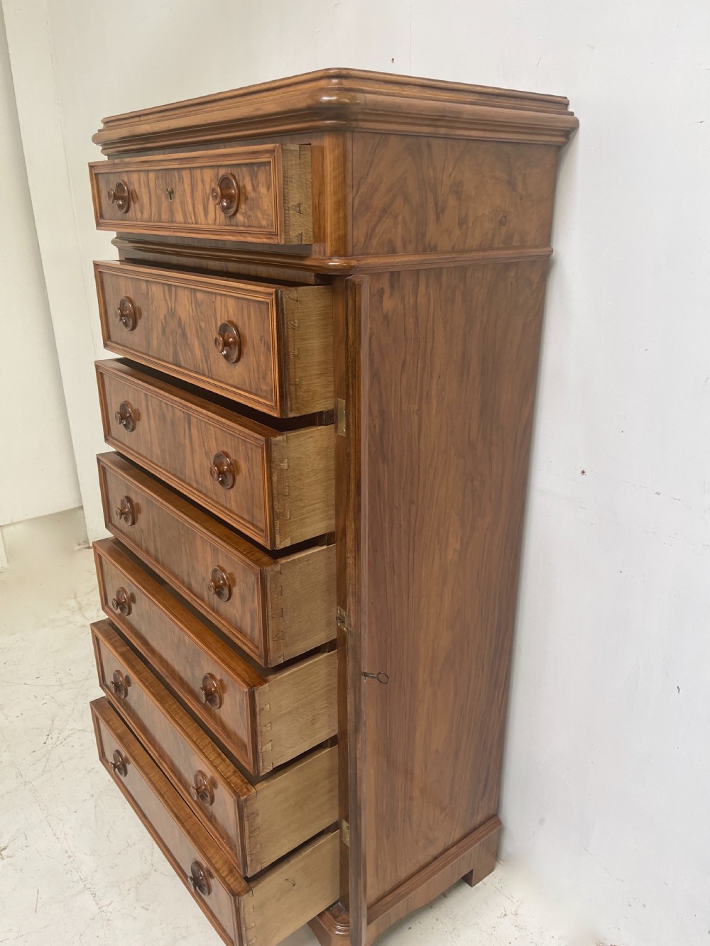 A tall Victorian walnut Wellington chest with seven graduated drawers, turned wooden knobs, and a hinged side-locking bar. View III
