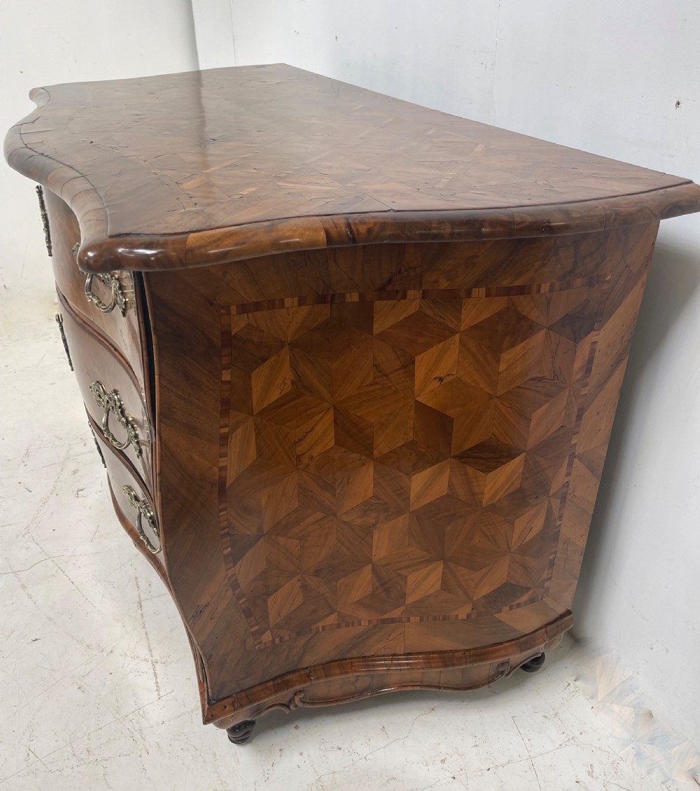 An 18th-century French bombe commode featuring three drawers with geometric parquetry inlay, a serpentine silhouette, and ornate brass handles. View II