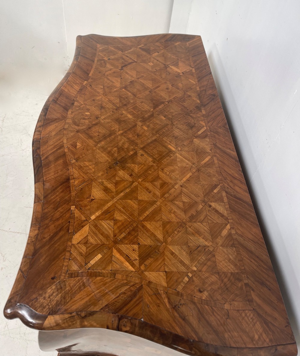 An 18th-century French bombe commode featuring three drawers with geometric parquetry inlay, a serpentine silhouette, and ornate brass handles. View III