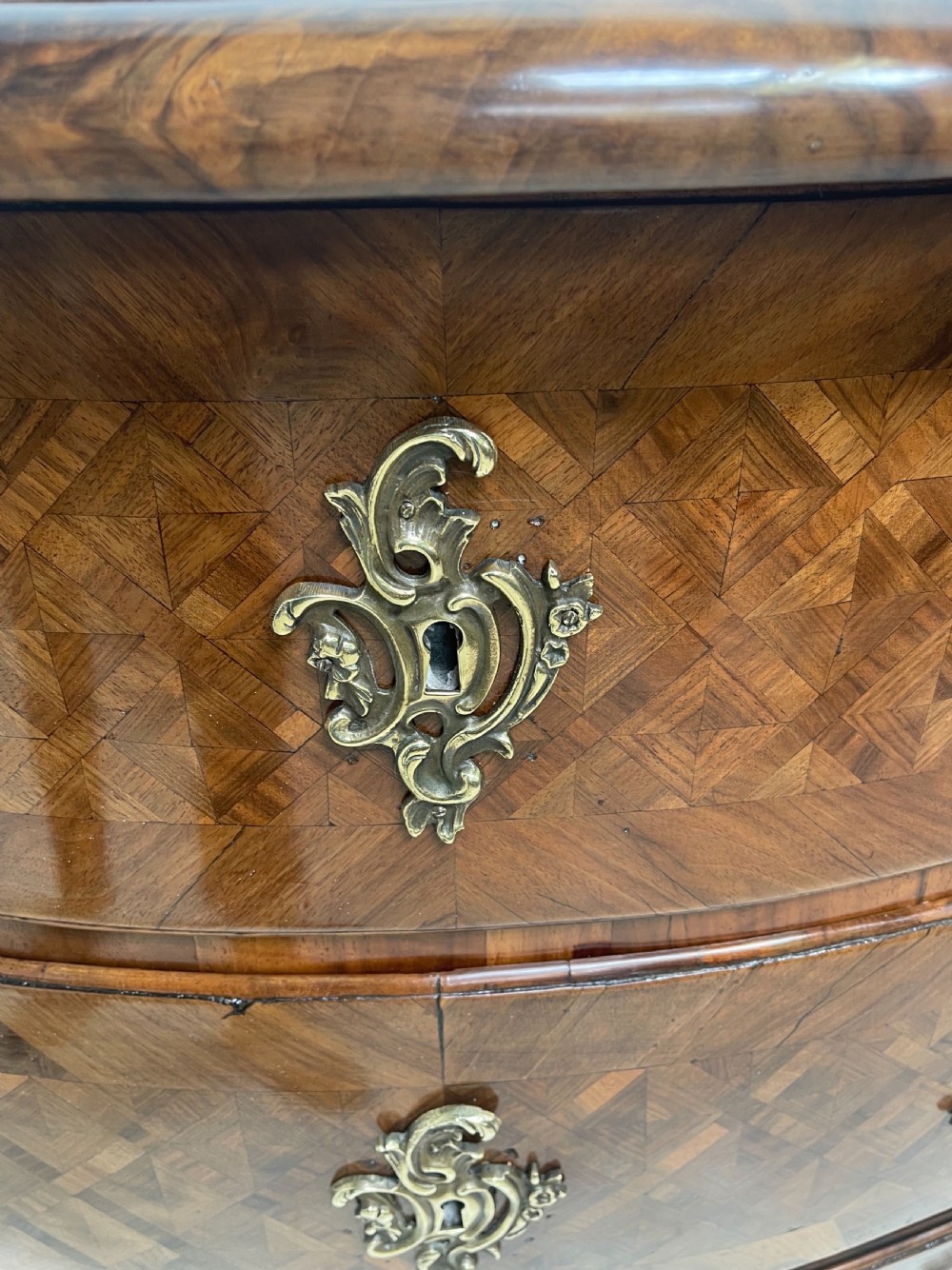 An 18th-century French bombe commode featuring three drawers with geometric parquetry inlay, a serpentine silhouette, and ornate brass handles. View VII