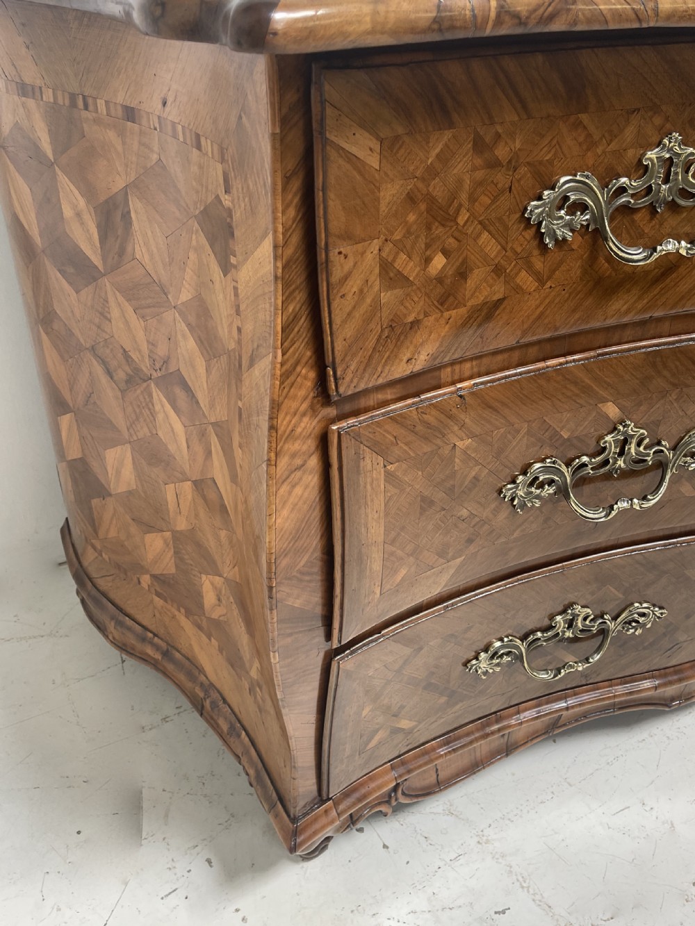 An 18th-century French bombe commode featuring three drawers with geometric parquetry inlay, a serpentine silhouette, and ornate brass handles. View VIII