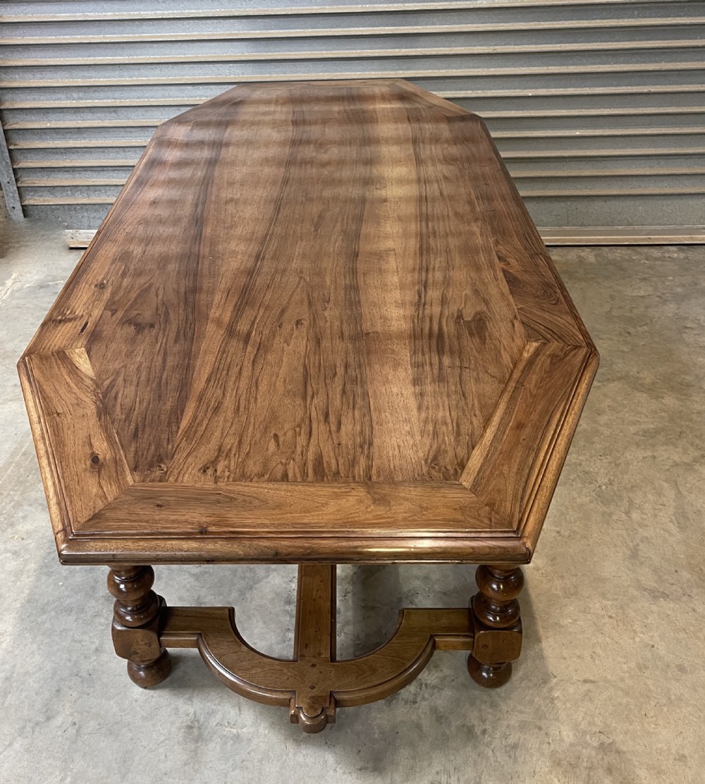 A long French walnut dining table featuring a shaped top with framed grain panels, turned legs, and a sculpted cross-stretcher.