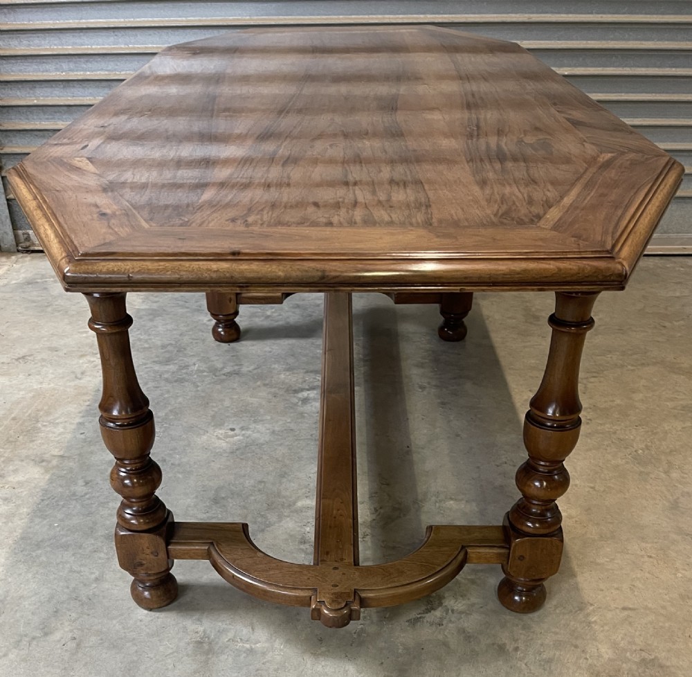 A long French walnut dining table featuring a shaped top with framed grain panels, turned legs, and a sculpted cross-stretcher. View II
