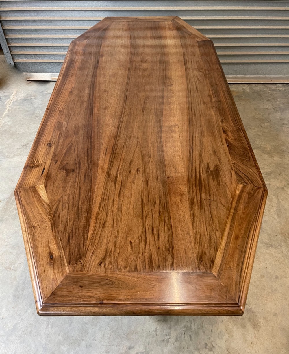 A long French walnut dining table featuring a shaped top with framed grain panels, turned legs, and a sculpted cross-stretcher. View III