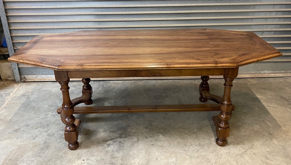A long French walnut dining table featuring a shaped top with framed grain panels, turned legs, and a sculpted cross-stretcher. View IV