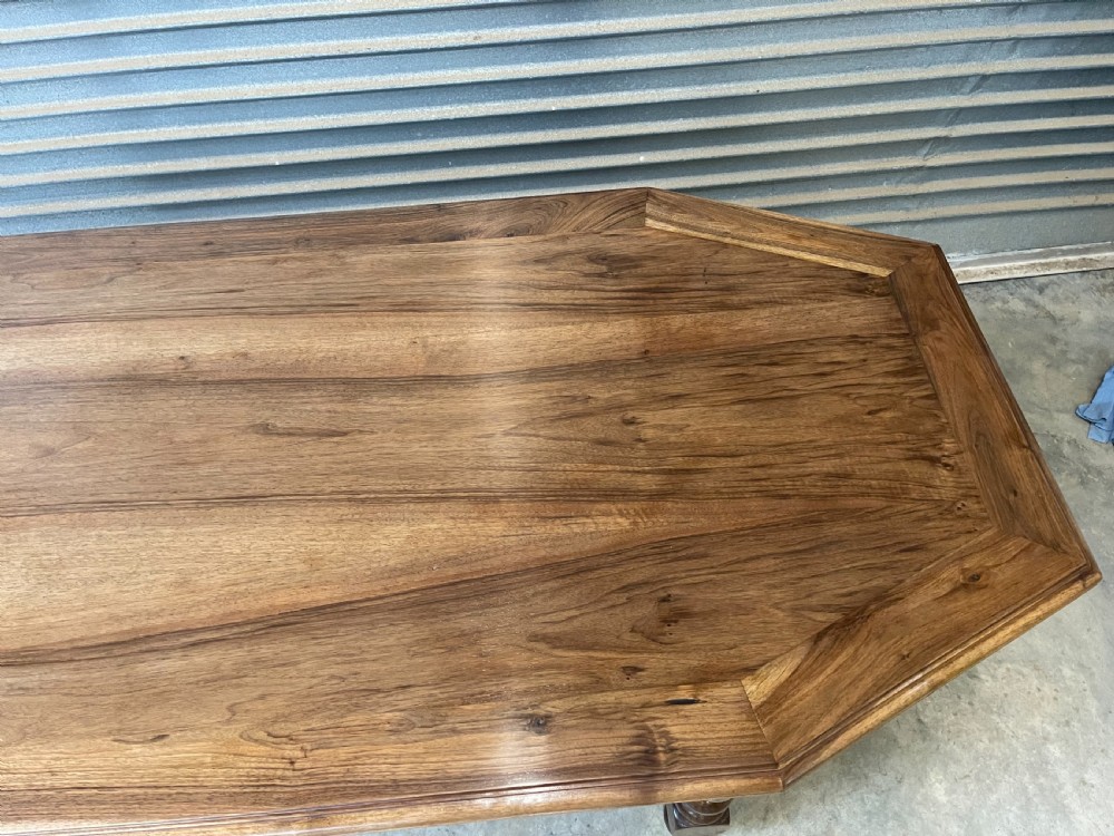 A long French walnut dining table featuring a shaped top with framed grain panels, turned legs, and a sculpted cross-stretcher. View V