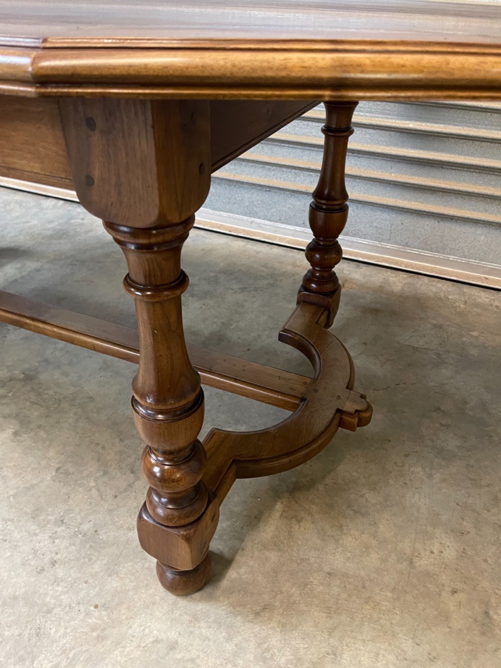 A long French walnut dining table featuring a shaped top with framed grain panels, turned legs, and a sculpted cross-stretcher. View VII