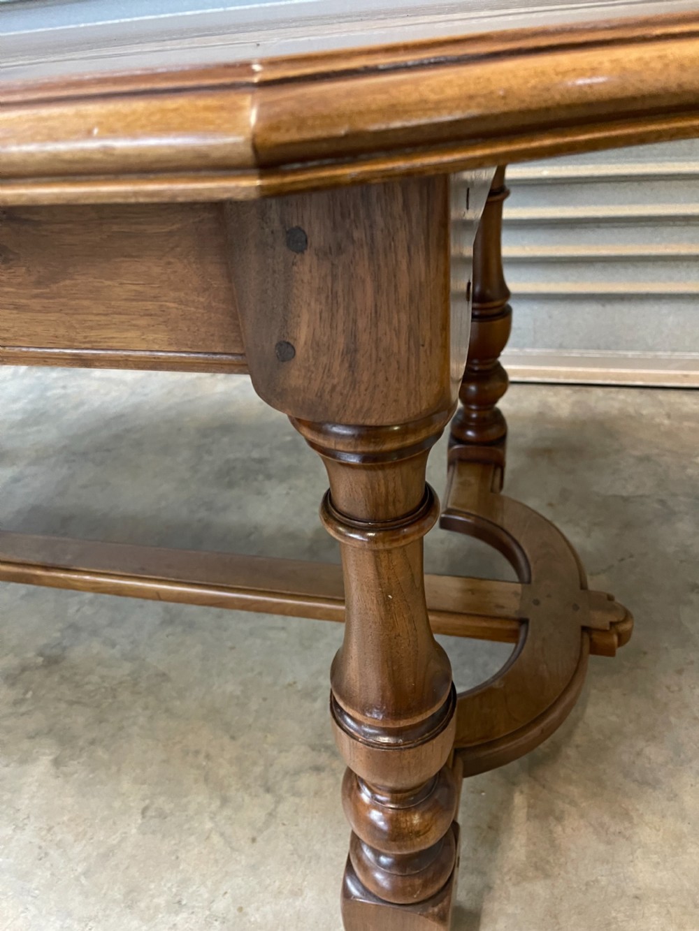 A long French walnut dining table featuring a shaped top with framed grain panels, turned legs, and a sculpted cross-stretcher. View IX
