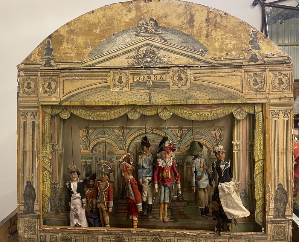 An antique wooden and paper toy puppet theatre labelled Opera, featuring miniature costumed marionettes on a painted classical stage. View III