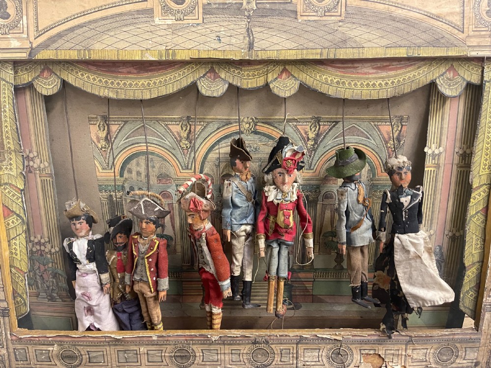 An antique wooden and paper toy puppet theatre labelled Opera, featuring miniature costumed marionettes on a painted classical stage. View VI