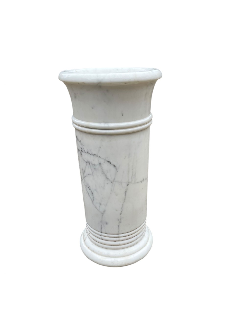 A cylindrical white marble umbrella stand with grey veining, flared rim, and reeded banding details.