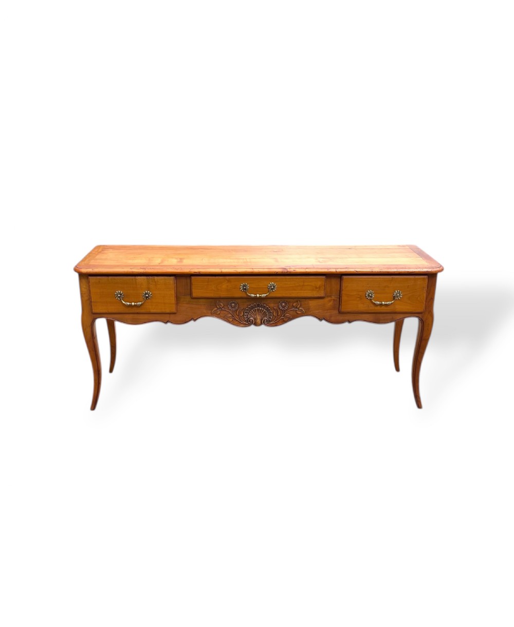 A French provincial cherrywood serving table featuring three drawers with brass drop handles, a hand-carved central shell motif on the apron, and slender cabriole legs.