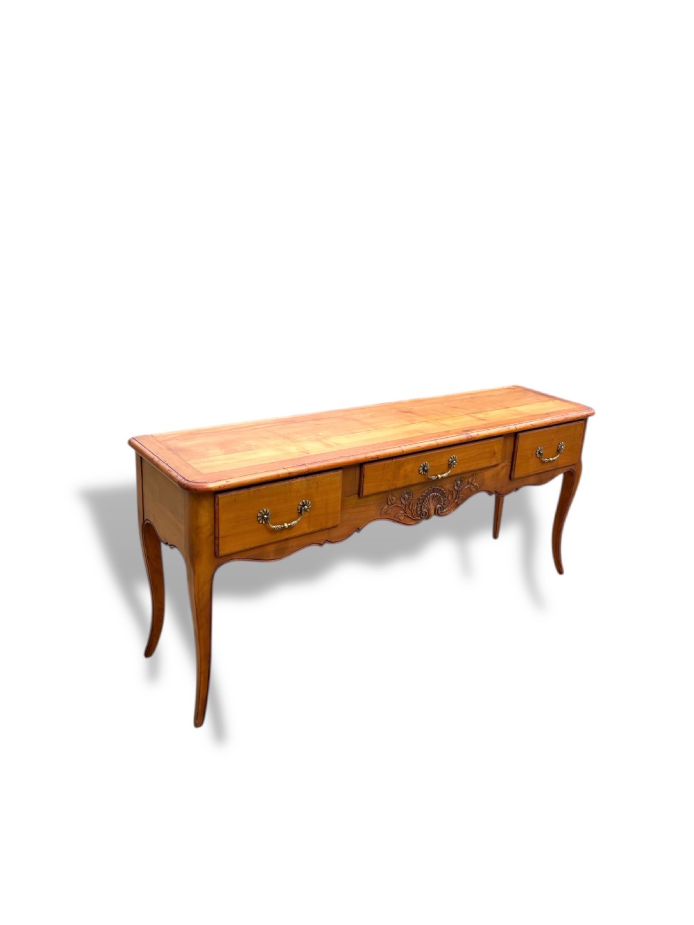 A French provincial cherrywood serving table featuring three drawers with brass drop handles, a hand-carved central shell motif on the apron, and slender cabriole legs. View II