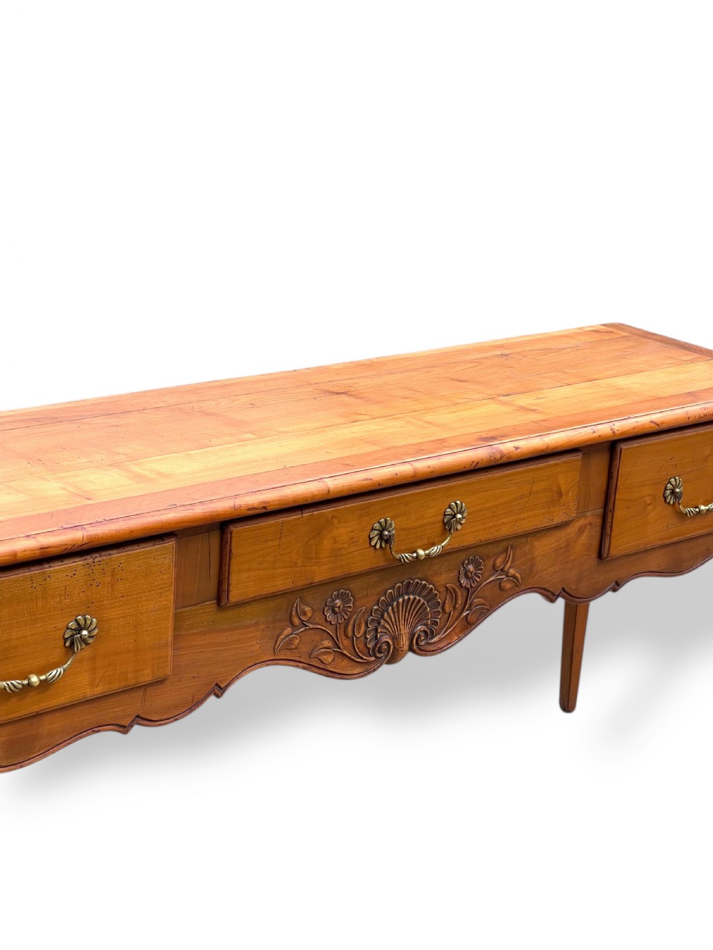 A French provincial cherrywood serving table featuring three drawers with brass drop handles, a hand-carved central shell motif on the apron, and slender cabriole legs. View III