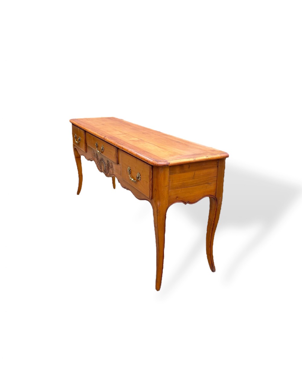 A French provincial cherrywood serving table featuring three drawers with brass drop handles, a hand-carved central shell motif on the apron, and slender cabriole legs. View VI