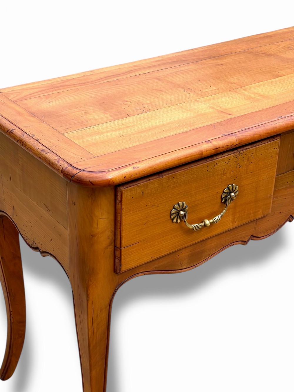 A French provincial cherrywood serving table featuring three drawers with brass drop handles, a hand-carved central shell motif on the apron, and slender cabriole legs. View VII