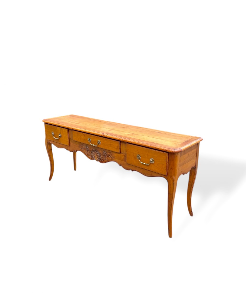 A French provincial cherrywood serving table featuring three drawers with brass drop handles, a hand-carved central shell motif on the apron, and slender cabriole legs. View XI