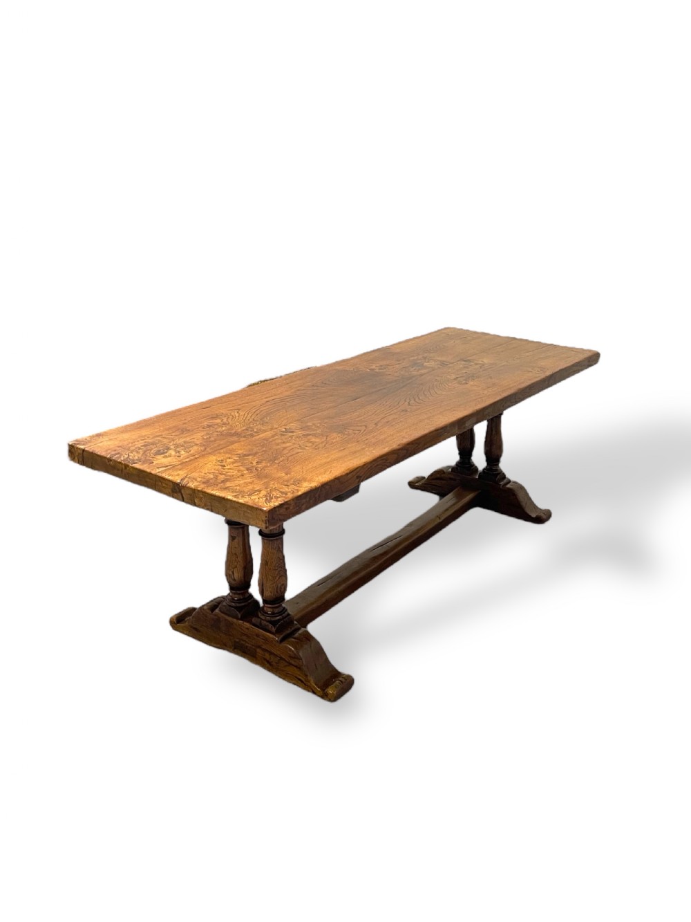 A solid warm brown oak refectory dining table featuring a thick rectangular top supported by double turned columns and a central stretcher.