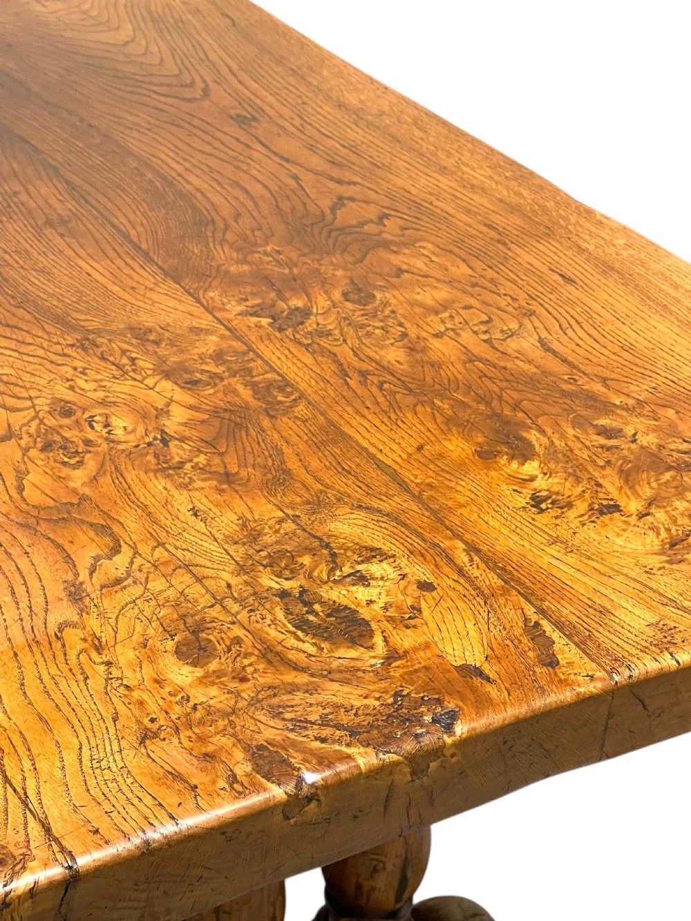 A solid warm brown oak refectory dining table featuring a thick rectangular top supported by double turned columns and a central stretcher. View V